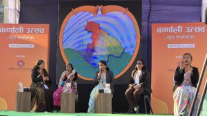 A panel discussion at the Karnali Utsav event, organized by the HRITI Foundation, featuring five women on stage, including a sign language interpreter. A large digital screen behind them displays a colorful map of the Karnali region inside a heart-shaped frame.