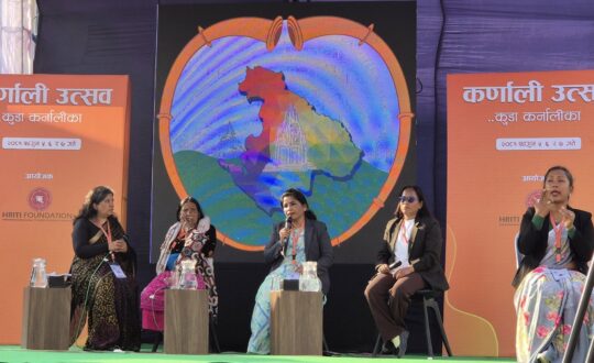 A panel discussion at the Karnali Utsav event, organized by the HRITI Foundation, featuring five women on stage, including a sign language interpreter. A large digital screen behind them displays a colorful map of the Karnali region inside a heart-shaped frame.